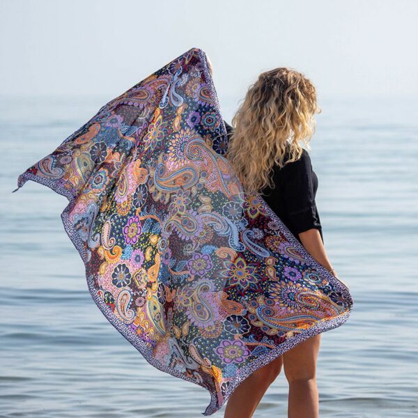 Beach scene of lady holding a multi coloured paisley print satin scarf