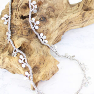 Silver metal long necklace with discs displayed on a piece of driftwood