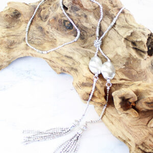 silver coloured long necklace with metal nuggets and silver tassles displayed on a piece of driftwood