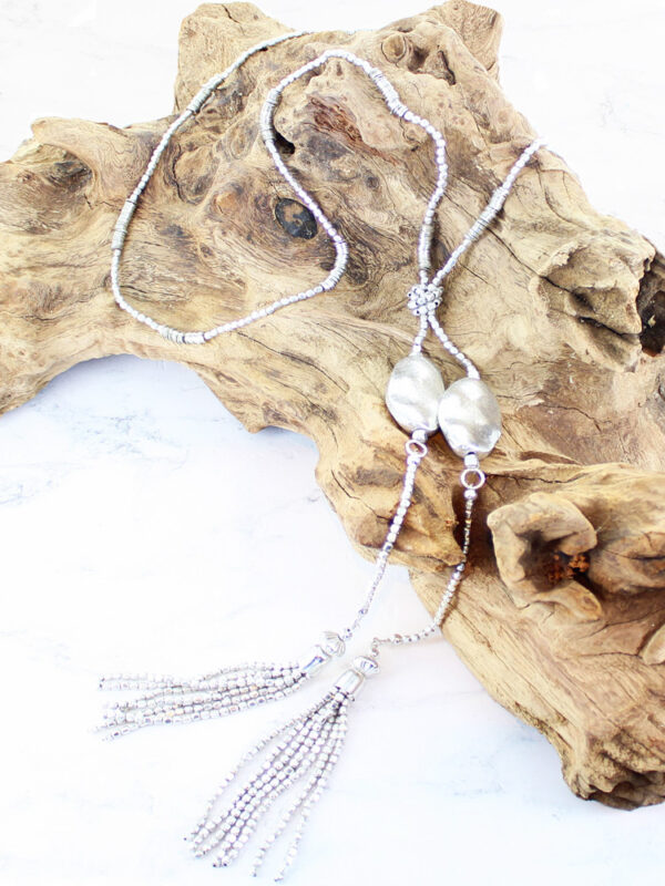 silver coloured long necklace with metal nuggets and silver tassles displayed on a piece of driftwood