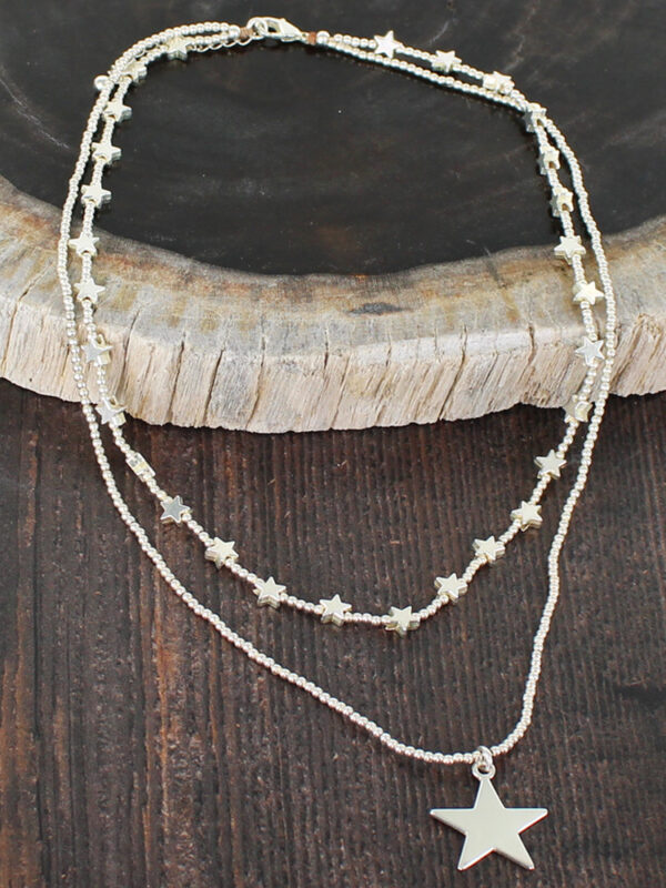 Double strand silver necklaces with stars on a brown background with a wooden display tile