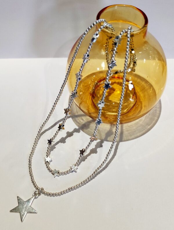 a two strand silver star necklace on a white background with a yellow glass bud vase