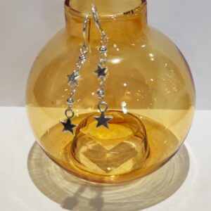Silver star earrings hanging from a yellow glass round bud vase