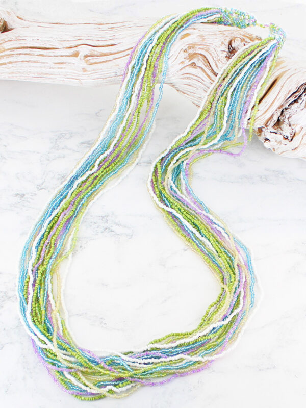 A long glass bead necklace in lilac, turquoise and lime green lying on a piece of driftwood