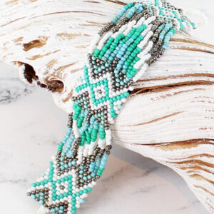 a blue and white glass bead bracelet threaded in an Aztec design, lying across a piece of white driftwood