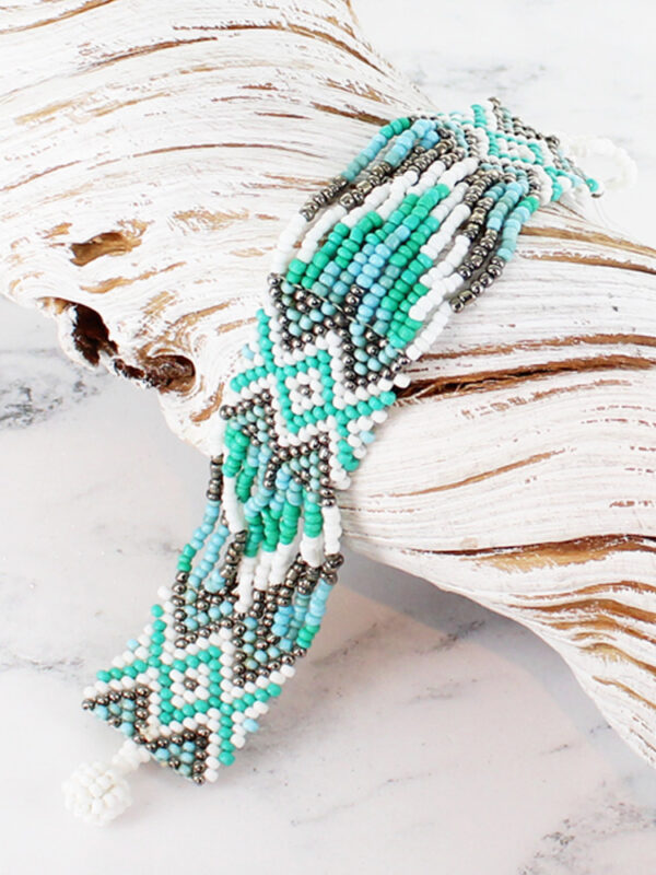 a blue and white glass bead bracelet threaded in an Aztec design, lying across a piece of white driftwood