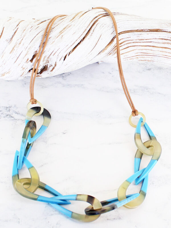 a long necklace made of resin and horn teardrop shapes linked together, lying on a piece of white driftwood
