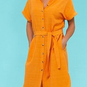 a blond lady wearing a mango coloured button thru kneelength shirtdress with a tie belt against a blue background