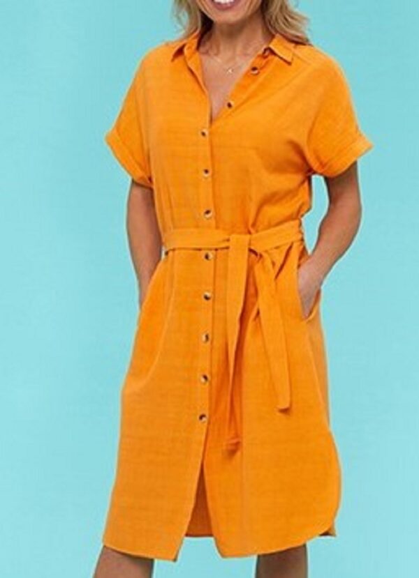 a blond lady wearing a mango coloured button thru kneelength shirtdress with a tie belt against a blue background