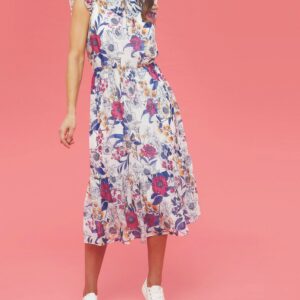 A dark haired lady against a pink background, wearing a white chiffon dress with a botanical print in blue and red worn with white lace ups