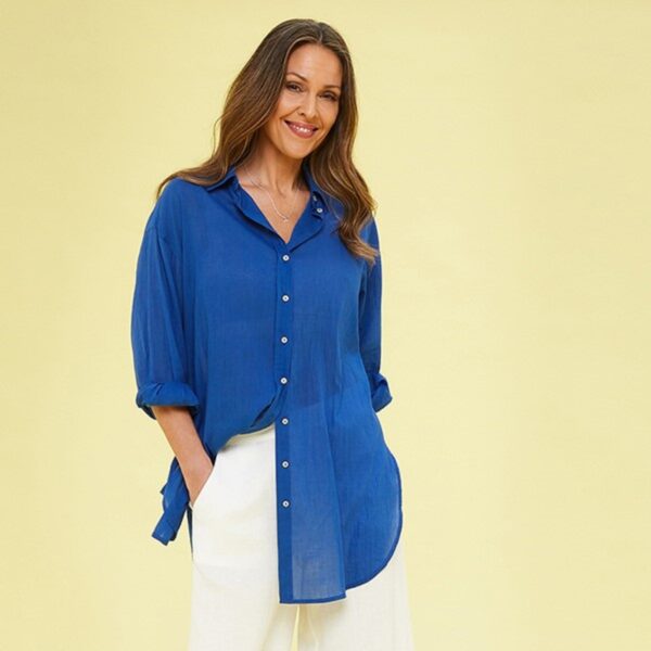 A lady with dark hair wearing a royal blue button front shirt and white trousers on a yellow background