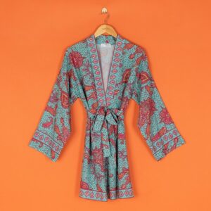 A short kimono in a red and turquoise paisley print hanging on a wooden hanger against an orange background