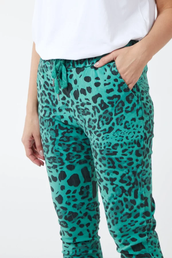 Lady wearing a white short sleeve tee shirt and green leopard print trousers with one hand in pocket and one hand by her side