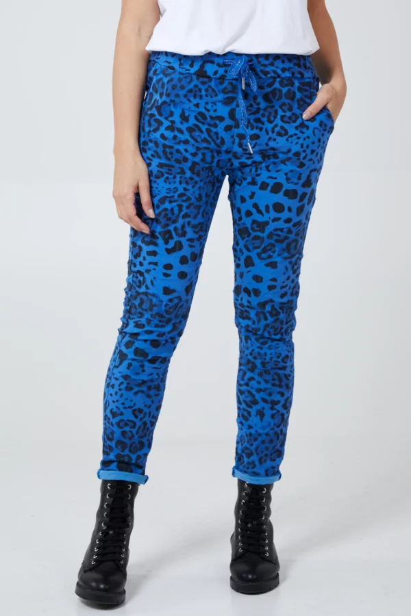 lady wearing a white short sleeve tee shirt, black lace up boots and royal blue leopard print trousers against a black white background