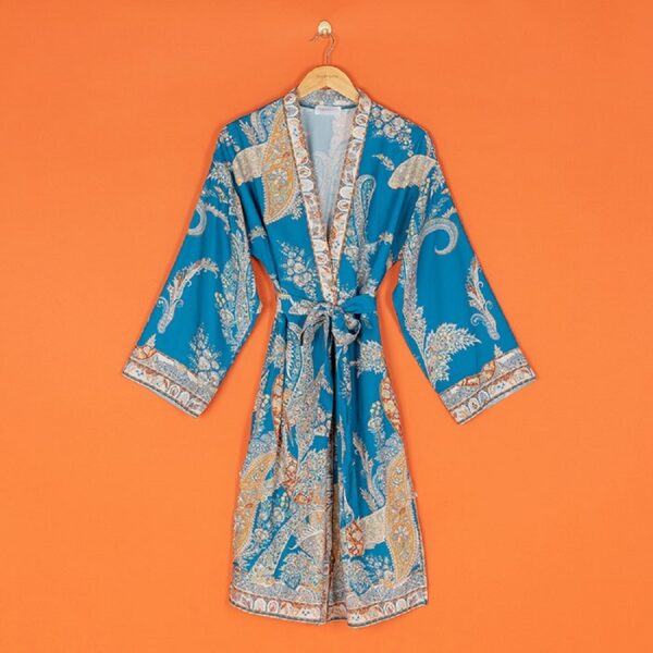 a blue paisley print kimono, hanging on a wooden hanger against an orange background