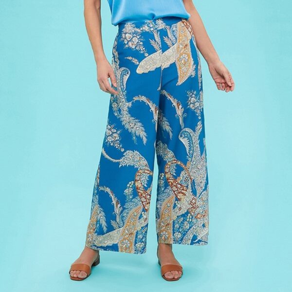 a lady wearing blue paisley printed wide legged palazzo style trousers and a blue satin lace trim camisole standing against a blue background