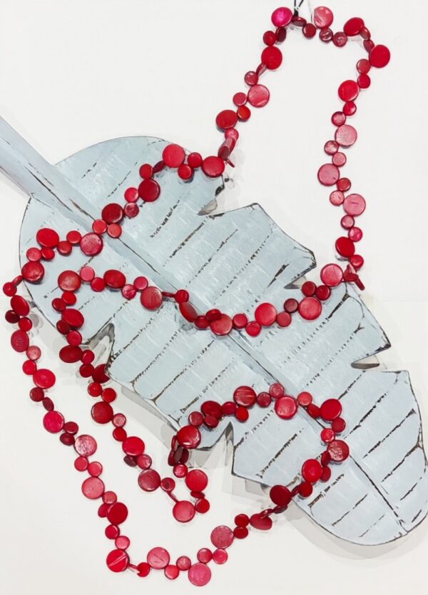 a very long necklace made of various sized coconut shell discs in a deep red colour. It is laid across a blue wooden leaf shaped dish