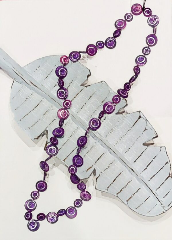 a long necklace made of purple coconut shell discs with a silver painted swirl on each disc, lying across a blue painted wooden leaf dish