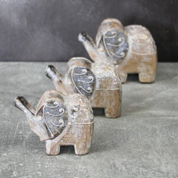 a set of 3 different sized handcarved elephants in white and gold distressed finish on a marble table