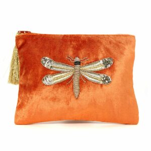 an orange velvet cosmetic bag with a large gold embroidered dragonfly on the front side and finished with a large gold tassle on the end of the zip
