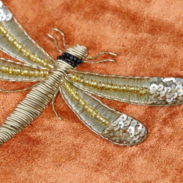 detail of a stylised embroidered dragonfly in gold thread on a burnt orange velvet ground