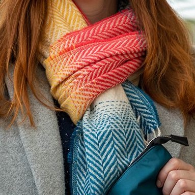 a lady with red hair wearing a grey wool coat and herringbone weave scarf in shades of red, blue and yellow
