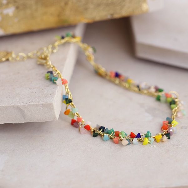 a gold chain bracelet with tiny multicoloured stone chips hanging from it, lying flat on some white blocks