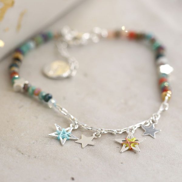 a little silver link bracelet made up of coloured stones and silver stars which have a stitched thread design on them. On a buff coloured background