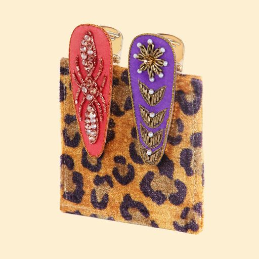 a set of two hairclips one orange with a jewelled knot design and the other is purple with a jewelled flower design clipped onto a leopard print velvet card