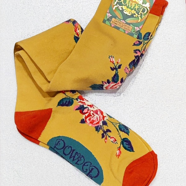 a pair of mustard coloured long socks folded on a white background, with orange toe and heel and pink roses on the front