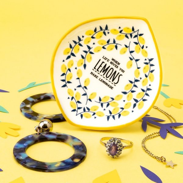 an image of a little flat trinket dish with the slogan'when life gives you lemons' inside a ring of yellow flowers on the surface, sitting on a yellow background with some earrings and a ring around it