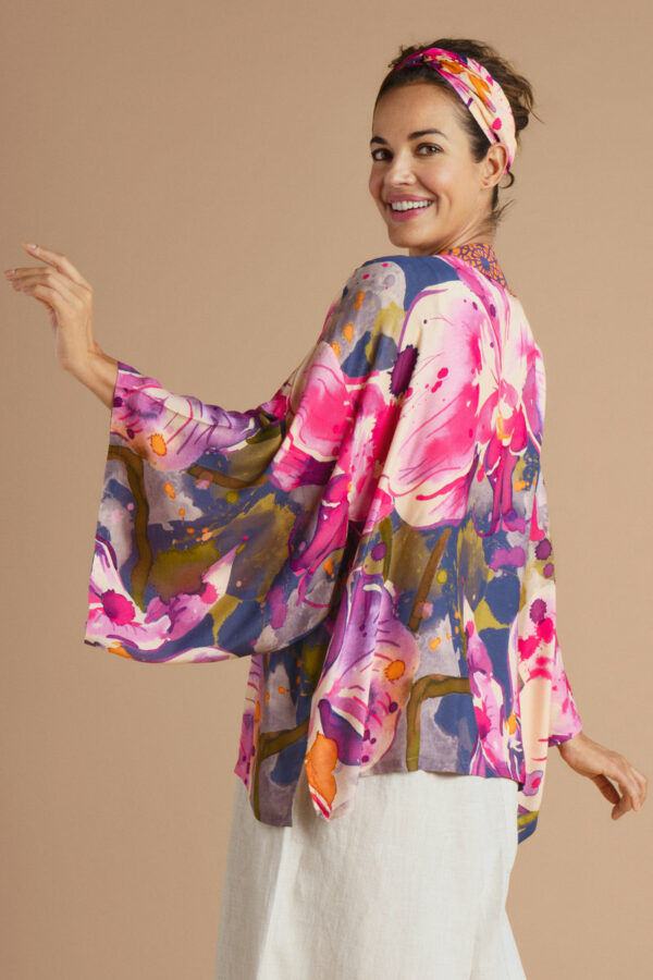 a girl wearing a short kimono jacket with a large abstract orchid print on it in pink, purple and navy