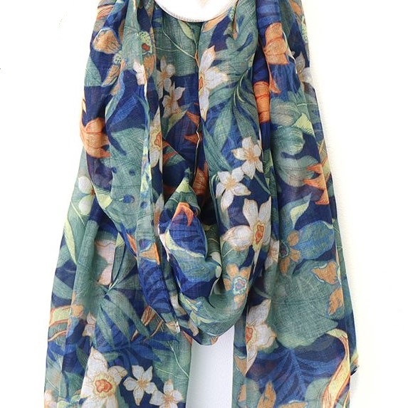 a recycled poly scarf with a print of leaves and flowers in green, peach and blue looped around a wooden hook