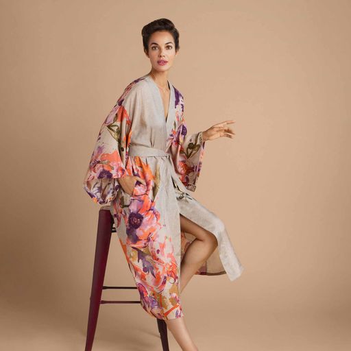 a girl sitting on a high stool wearing a coconut coloured long belted kimono with a print of orchids and lilies in purple, pink and orange
