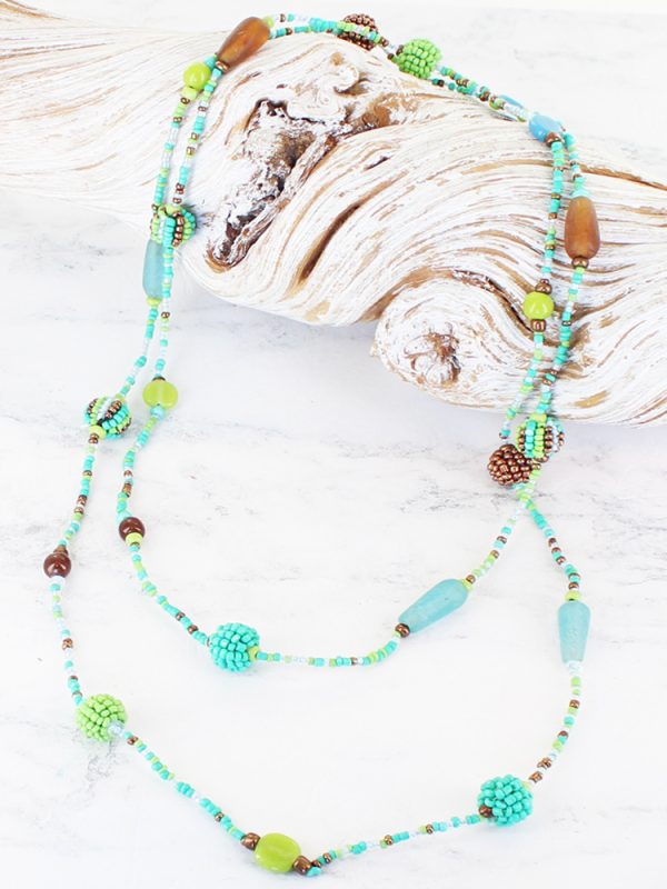 a beaded necklace with beads of assorted shapes and sizes, in apple green, aqua and turquoise, lying on a piece of white driftwood