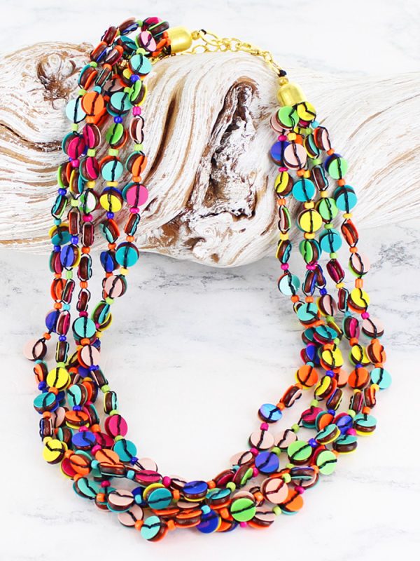 a multi strand necklace made up of strung together rainbow coloured sequins with gold metal fastening, lying on a piece of white driftwood