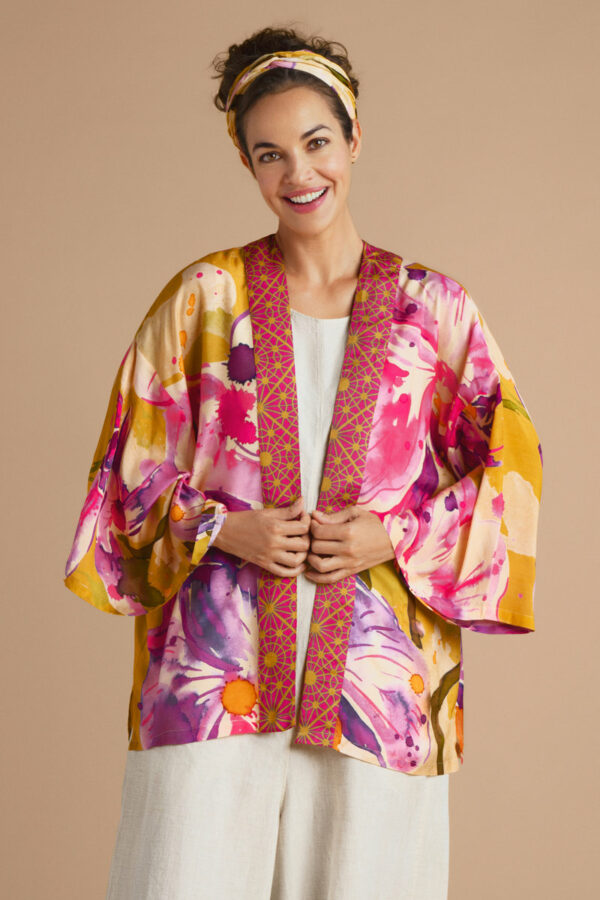 a girl in a white top and trousers wearing a short kimono in a floral orchid print in mustard and fucshia with contrast trim down the front