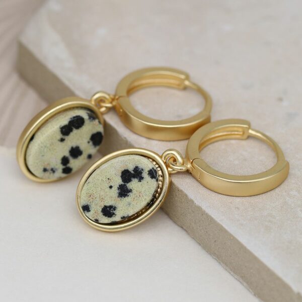 a small burnished gold coloured hoop earring with an oval dalmation jasper stone drop