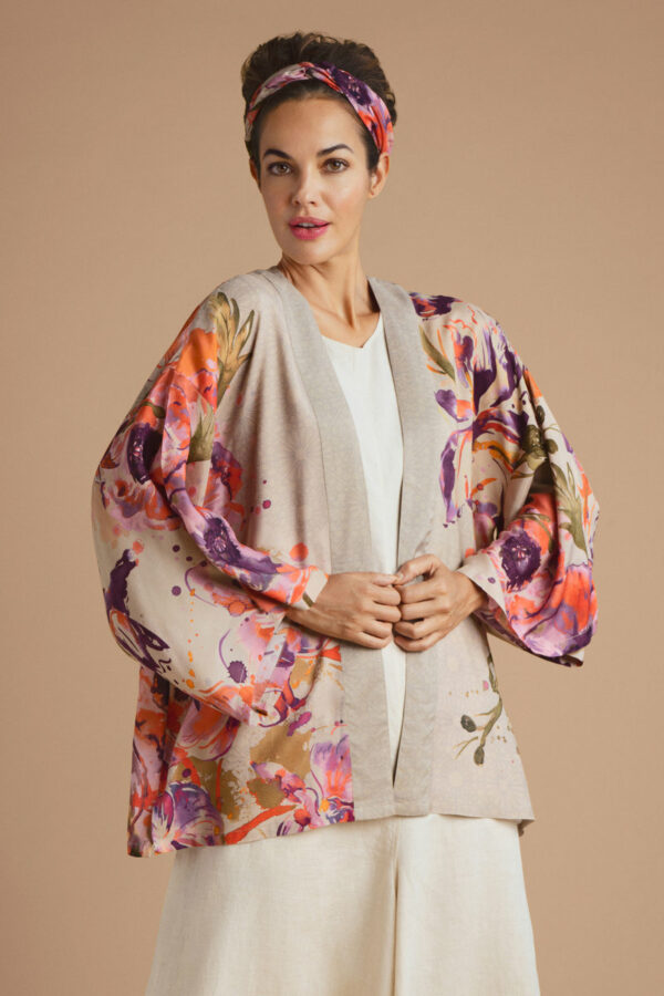 a girl in a short kimono style jacket in a base colour of coconut beige with an oversized abstract orchid print in orange and purple