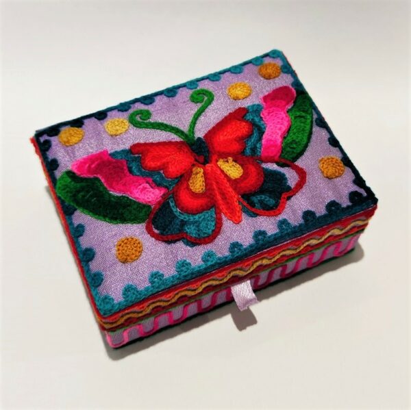 a small wooden jewellery box covered in lilac fabric and embroidered with a big butterfly on the lid with pink, green and red wings, decorated round the sides with pink, red and yellow border embroidery