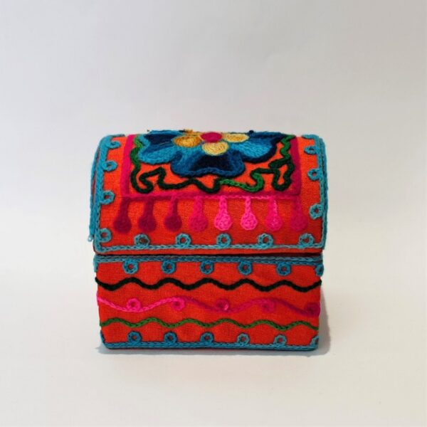 A mini box in orange fabric, embroidered all over with flowers and abstract lines in turquoise, pink, green and gold. A pull off lid with a domed top.