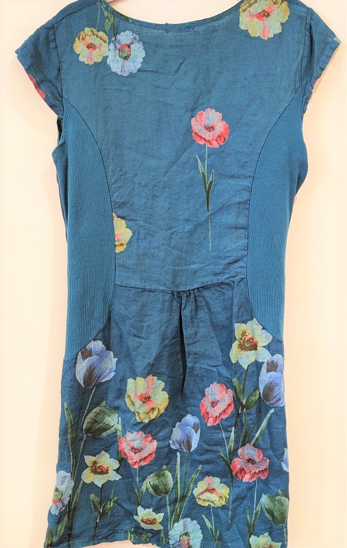 back view of a teal linen dress with ribbed jersey inset side panels and a flower print on the bottom half