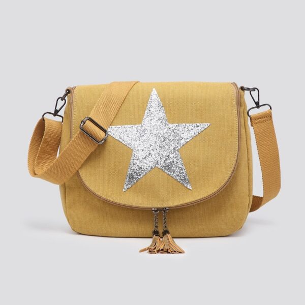 A mustard coloured cotton canvas crossbody messenger bag with a glittery silver star on the front flap and two tassles on the zip ends, with a self coloured webbing strap