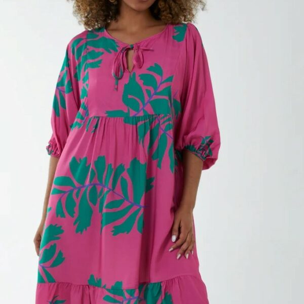a girl wearing a bright pink smock style dress with a jade green oversized leaf print. An open neck tied with a bow and balloon sleeves