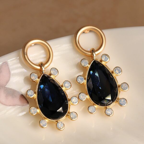 a deep blue sapphire drop earring surrounded by tiny white crystals, hanging from a gold circle top, and all plated in burnished gold.