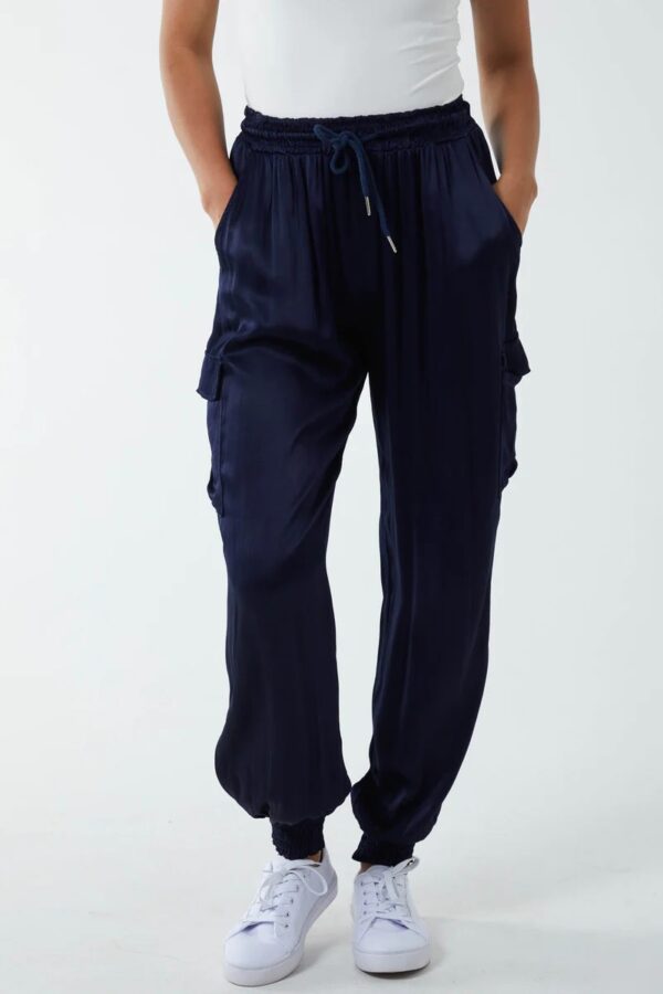 a pair of midnight navy satin cargo pants with two pockets on each side, an elasticated waistband and cuffs, worn with a white vest.