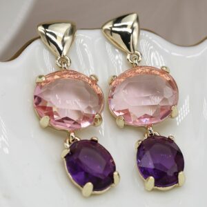 a pair of faux gold earrings on a white saucer - with a large pink crystal drop and a purple crystal drop hanging below
