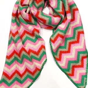 a knitted scarf with diagonal ends and a zig zag stripe pattern in pink, green and deep orange, with green blanket stitching on all sides